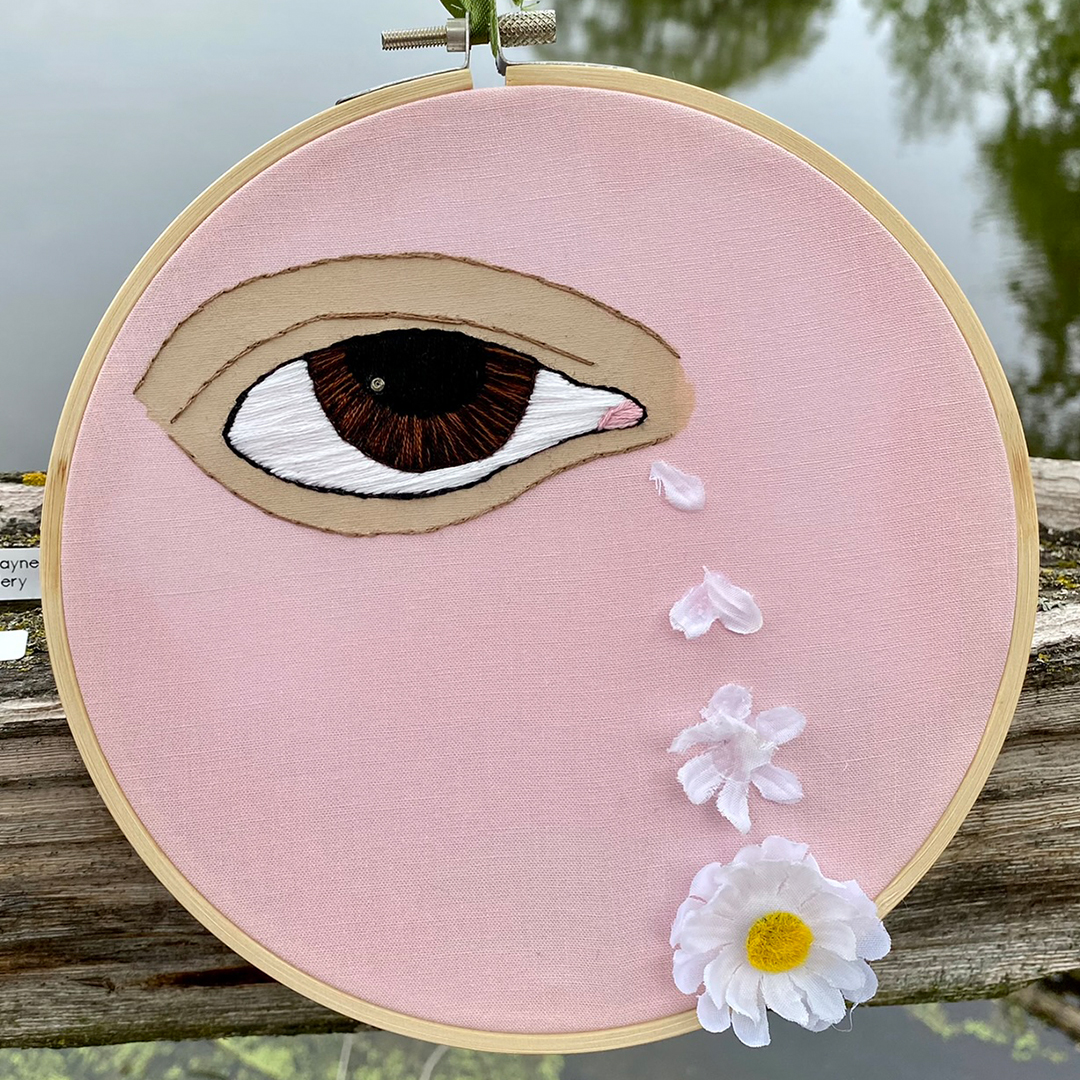 an embroidery of an eye crying tears that are flower petals